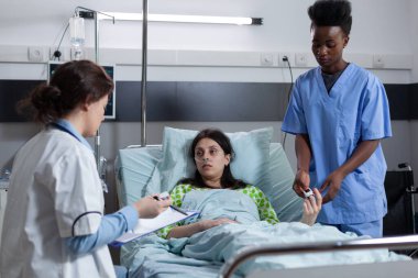 Doktor panoyu test sonuçlarıyla tutarken hemşire Spo2 izleme cihazı yerleştiriyor.