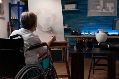 Tekerlekli sandalye kullanan kıdemli bir sanatçı. Durgun yaşam vazosunun orijinal çizimlerini çiziyor.