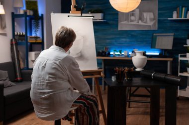 Yaşlı kadın, resim sehpasındaki vazonun yaratıcı çizimine bakarak ilham almış gibi hissediyor.