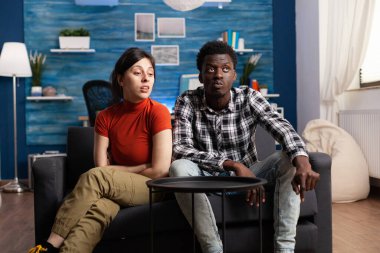 Oturma odasındaki kanepede oturan sinirli, çok ırklı genç çift.