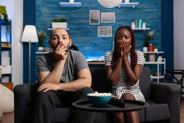 Casal interracial chocado assistindo notícias trágicas na TV — Fotografia de Stock