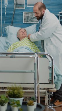 Doktor, hastane yatağında steteskop kullanıyor.