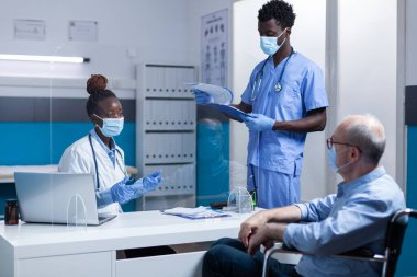 Klinik doktoru tekerlekli sandalyedeki yaşlı kişiye hastalık belirtilerini açıklıyor.