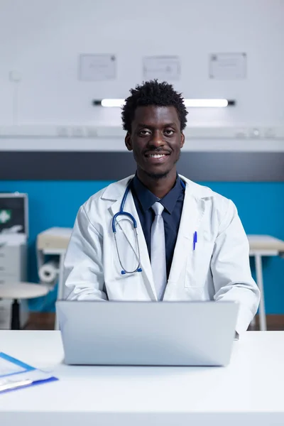 Smiling hospital doctor specialist sitting at clinic cabinet desk — Stock Photo, Image