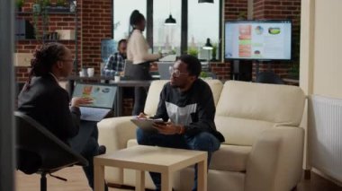 Kadın dizüstü bilgisayarda veri tablolarını açıklıyor ve adam not alıyor.