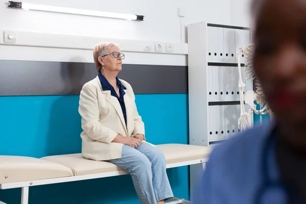 Відпущена старша жінка-пацієнтка, що стоїть на ліжку, чекає на знання хвороби під час медичного призначення — стокове фото