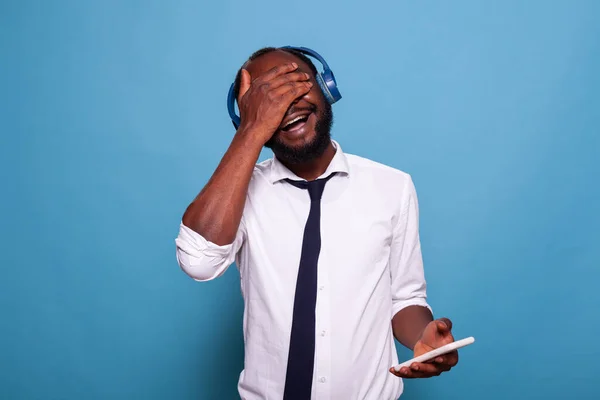 Mosolygós férfi gazdaság okostelefon borító szem tenyérrel véletlenszerűen válassza ki a dalt a lejátszási listából — Stock Fotó