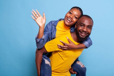 Mutlu adam kameraya el sallayan kadını sırtında taşıyor.