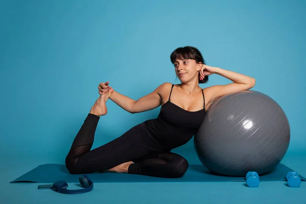 Ritratto di atleta donna seduta su un tappetino da yoga appoggiata allo yoga fitball — Foto Stock