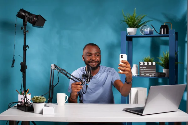 Vlogger seduto nello studio di vlogging con microfono che si fa un selfie con smartphone — Foto Stock