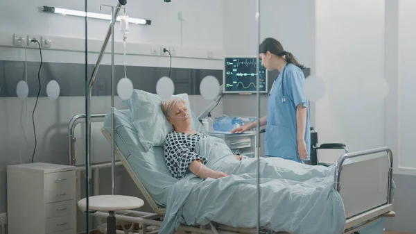 Női nővér ellenőrzi alvó idős beteg az ágyban — Stock Fotó
