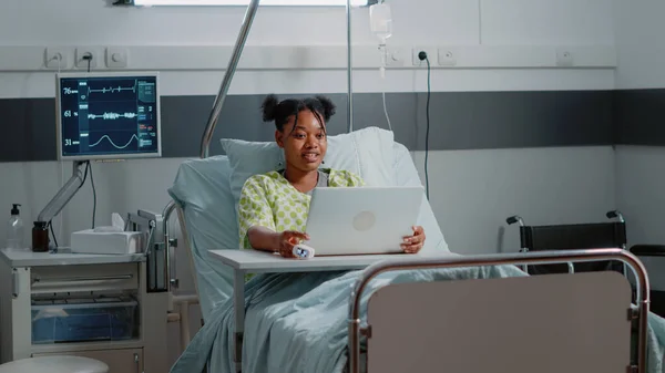 Jovem paciente usando chamada de vídeo no laptop moderno na cama — Fotografia de Stock