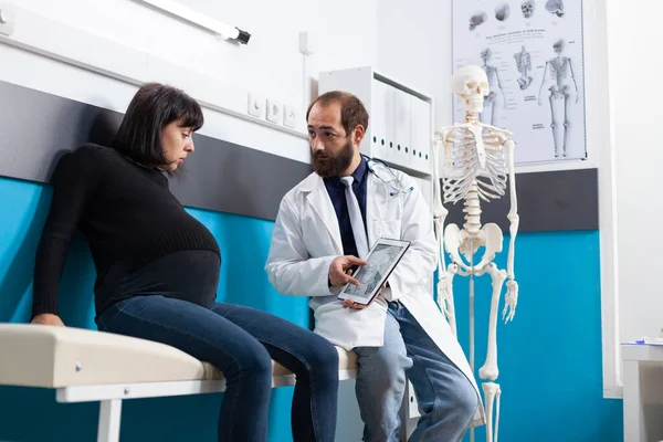 Obstetra mostrando esqueleto humano em comprimido digital para paciente — Fotografia de Stock