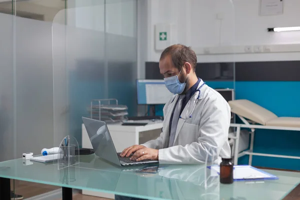 General practitioner with face mask and white coat using laptop — Stock Photo, Image