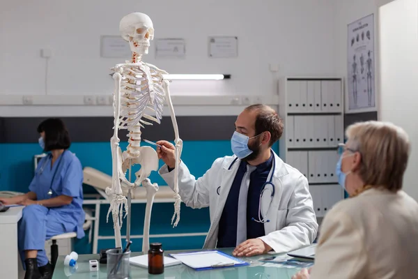 Specialist explaining human skeleton to retired woman at checkup visit — Stock Photo, Image