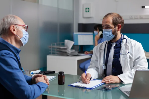 Doctor consulting volwassen man en het maken van aantekeningen bij checkup bezoek — Stockfoto