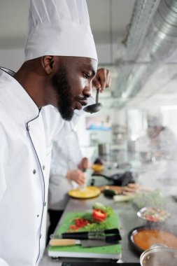 Afro-amerikan baş aşçı profesyonel mutfakta yemek pişirirken yemek servisi için gurme tadı alıyor..