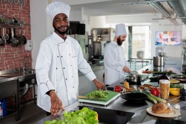 Yemek pişirme üniforması giyen usta bir aşçı restoran mutfağında yemek malzemeleri hazırlıyor..