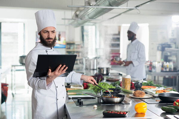 Head cook with computer brainstorming gourmet dish recipes for food contest held at restaurant.