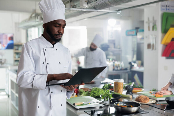 Gourmet cuisine head chef with laptop looking for gastronomic dish recipes and garnish ideas in restaurant kitchen.