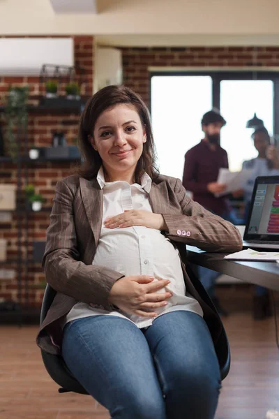 Sorrindo grávida empresa financeira empresária sentada na mesa no espaço de trabalho do escritório enquanto olha para a câmera. — Fotografia de Stock