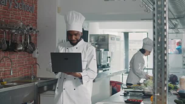 Африканський американець дивиться на екран ноутбука, щоб приготувати страву з гармат. — стокове відео