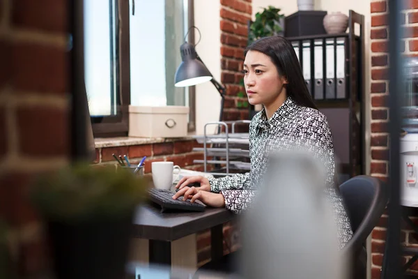 Självsäker kontor kvinnlig arbetare omsöka projekt marknadsföring idéer samtidigt som du använder arbetsdatorn och sitter vid skrivbordet. — Stockfoto