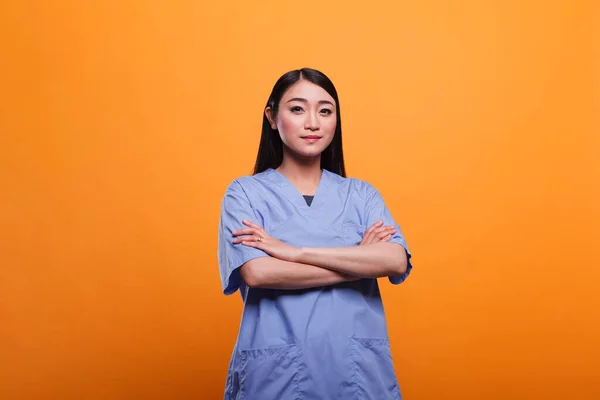 Pewny siebie i szczęśliwy pracownik szpitala azjatyckiego z rękami w kieszeniach, noszący odzież kliniczną. — Zdjęcie stockowe