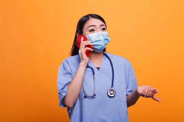 얼굴 문자와 청진기를 착용하고 스마트폰으로 환자와 이야기하는 젊은 아시아 출신 간호사. — 스톡 사진