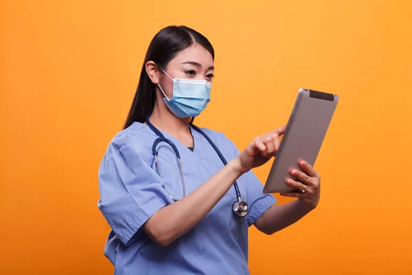 Infermiere medico fiducioso e responsabile che indossa maschera facciale e stetoscopio utilizzando tablet touchscreen. — Foto Stock