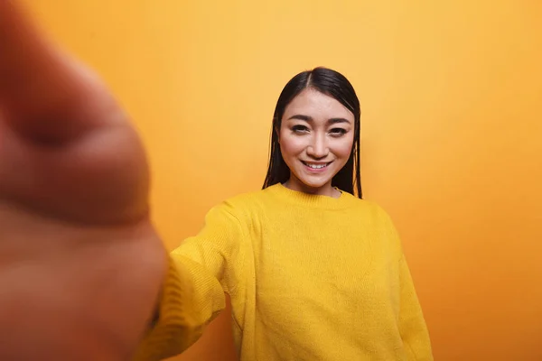 POV de sourire heureux influenceur portant pull jaune prendre selfie avec caméra tandis que sur fond orange. — Photo
