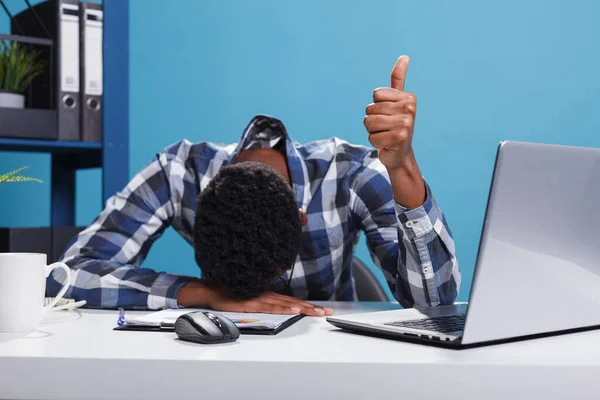 Exhausted young adult businessman falling asleep on desk while showing thumbs up gesture with hand. — Stock Photo, Image