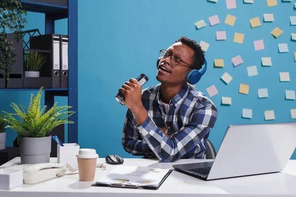 Χαρούμενος χαμογελαστός νέος υπάλληλος γραφείου που φοράει ασύρματα ακουστικά και ακούει μουσική — Φωτογραφία Αρχείου
