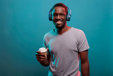 Genç adam kahve tutuyor ve kulaklıkla müzik dinliyor.