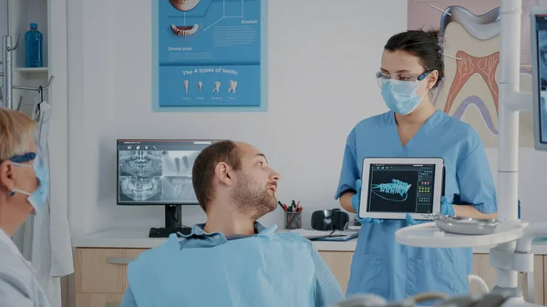 Стоматологическая бригада, указывающая на рентгенографию протезов на планшете — стоковое фото