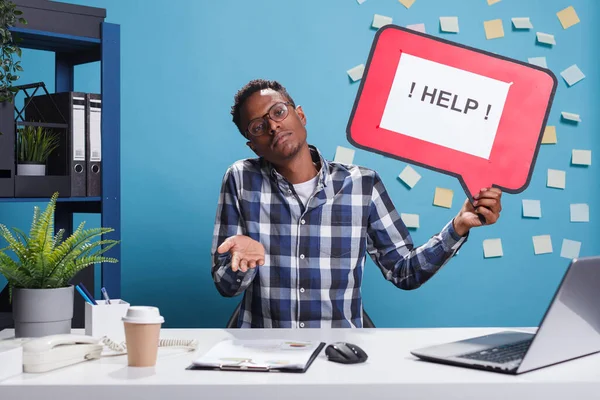 Összezavarodott és tudatlan vállalati irodai dolgozó kezében segítség karton buborék jel, miközben vállat vonva a munkahelyen. — Stock Fotó