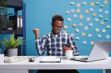 Heyecanlı genç iş adamı, zafer jesti yaparken akıllı telefon oyununu kazanmayı kutluyor..