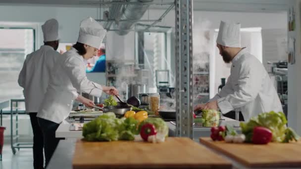 Vrouw in uniform koken heerlijke schotel op keukenfornuis — Stockvideo