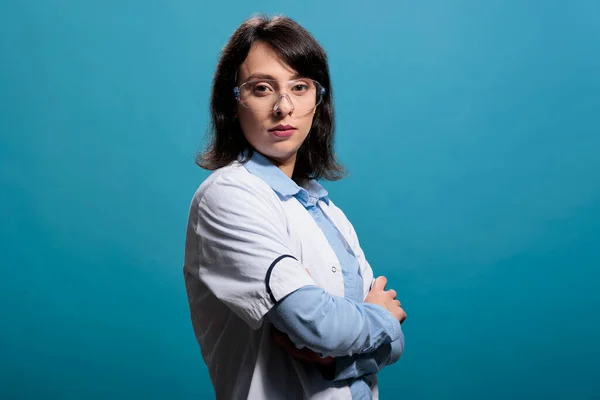 Biochemicus wetenschapper expert in het dragen van labjas en beschermende bril, staande op blauwe achtergrond — Stockfoto