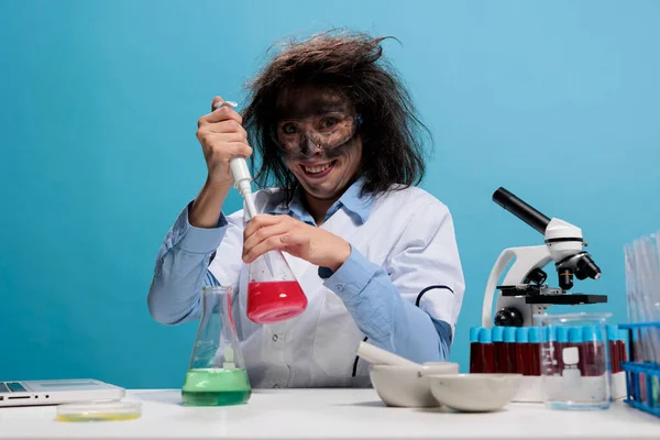 미친 것처럼 보이는 화학자가 화학 폭발 후에 드로퍼를 사용하여 실험실에서 일하는 동안 카메라 앞에서 소름끼치게 웃는다. — 스톡 사진