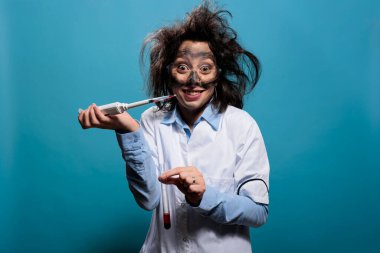 Pipetten cam test tüpüne zehirli bileşik damlatırken ürkünç sırıtan çılgın bir laboratuar çalışanı.