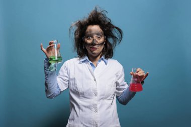 Mavi arka planda bilinmeyen kimyasal bileşiklerle dolu Erlenmeyer cam kavanozlarını tutan çılgın görünümlü kimyager..