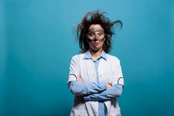 Humoristische gekke wetenschapper met grillig haar en smerig gezicht staande met gekruiste armen. — Stockfoto