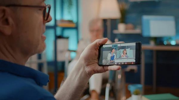 Důchodce držící smartphone pro použití vzdálené videokonference — Stock fotografie