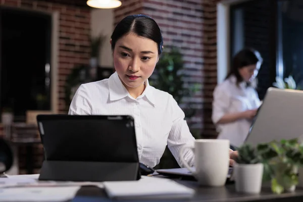 Donna d'affari asiatica con tablet moderno che rivede la documentazione contabile nello spazio di lavoro dell'ufficio. — Foto Stock