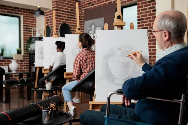 Homem paralisado sênior em cadeira de rodas atacando vaso de desenho de classe de arte — Fotografia de Stock