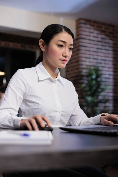 Portrait shot of confident businesswoman at night sitting in office workspace while working on laptop. — Stock Photo, Image