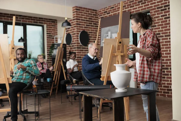Professor de pintura supervisionando o homem idoso enquanto desenha o modelo de vaso na tela — Fotografia de Stock