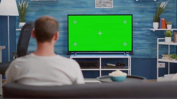 Man zit op de bank en kijkt naar groen scherm op tv en schakelt van kanaal — Stockvideo
