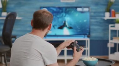 Kanepede otururken elinde kablosuz kontrol cihazı olan bir adam TV 'de oyun oynuyor.